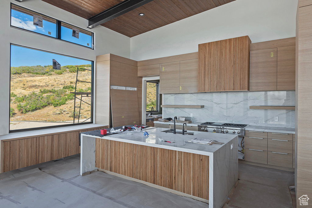 Kitchen featuring an island with sink, tasteful backsplash, high end stove, wooden ceiling, and sink