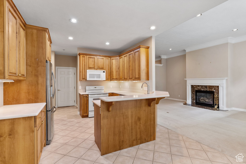 Kitchen featuring a high end fireplace, white appliances, light carpet, a breakfast bar, and kitchen peninsula