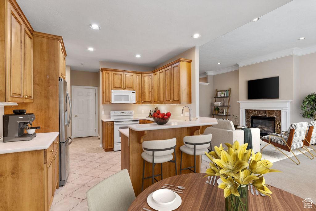 Kitchen with a fireplace, ornamental molding, white appliances, a kitchen bar, and kitchen peninsula