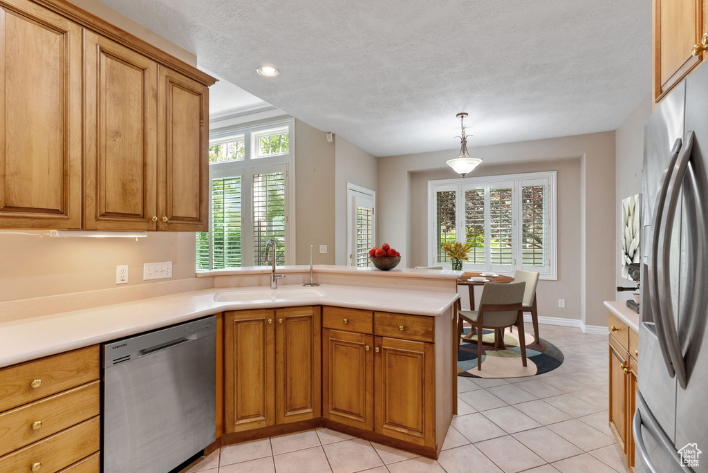 Kitchen featuring decorative light fixtures, light tile patterned floors, kitchen peninsula, sink, and appliances with stainless steel finishes