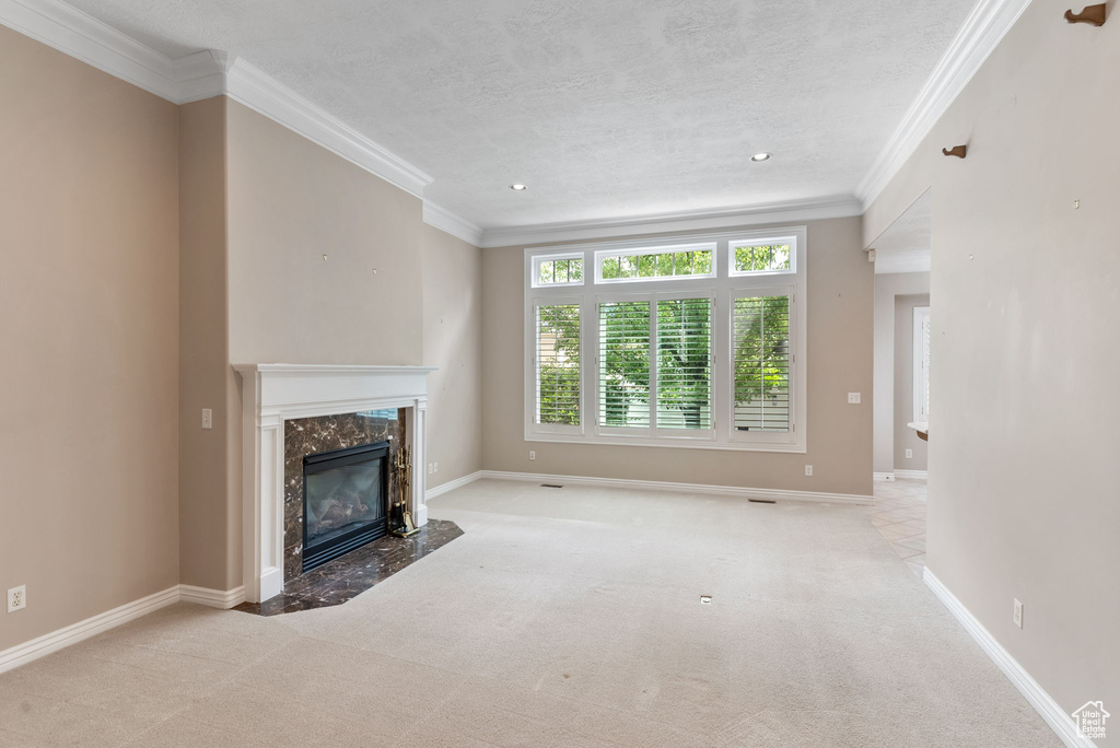 Unfurnished living room with a textured ceiling, crown molding, light carpet, and a fireplace