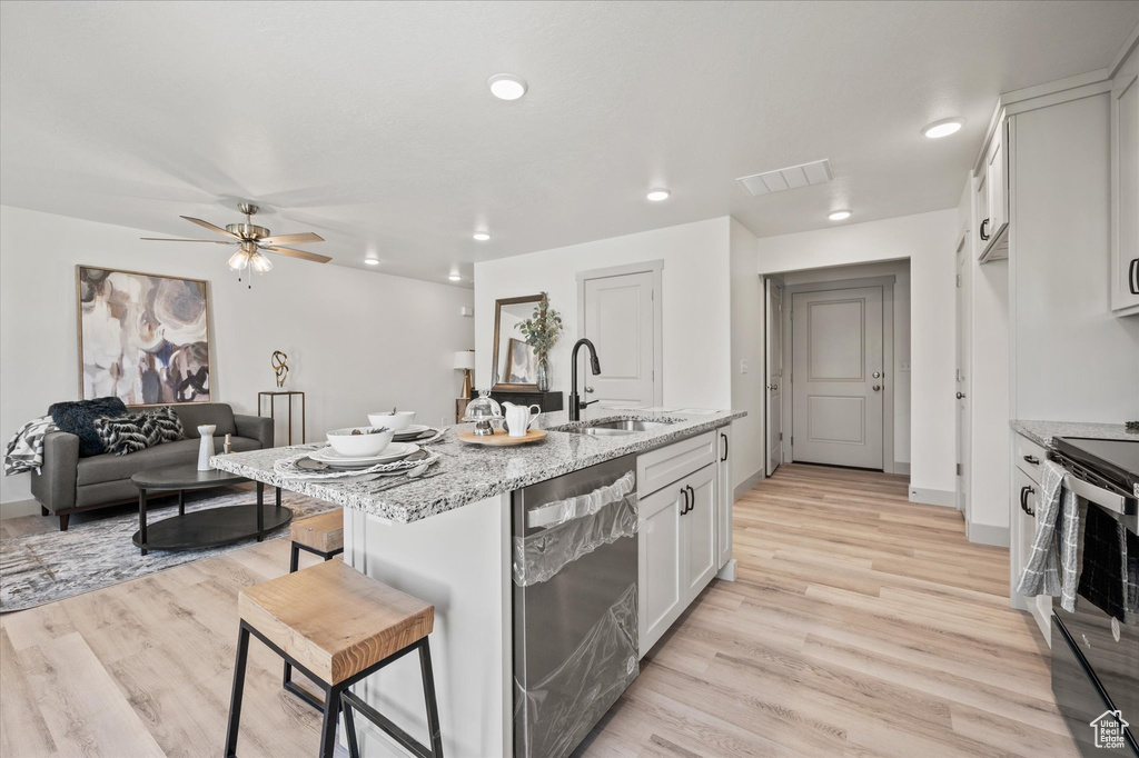 Kitchen featuring white cabinetry, sink, light stone counters, a breakfast bar area, and stainless steel dishwasher