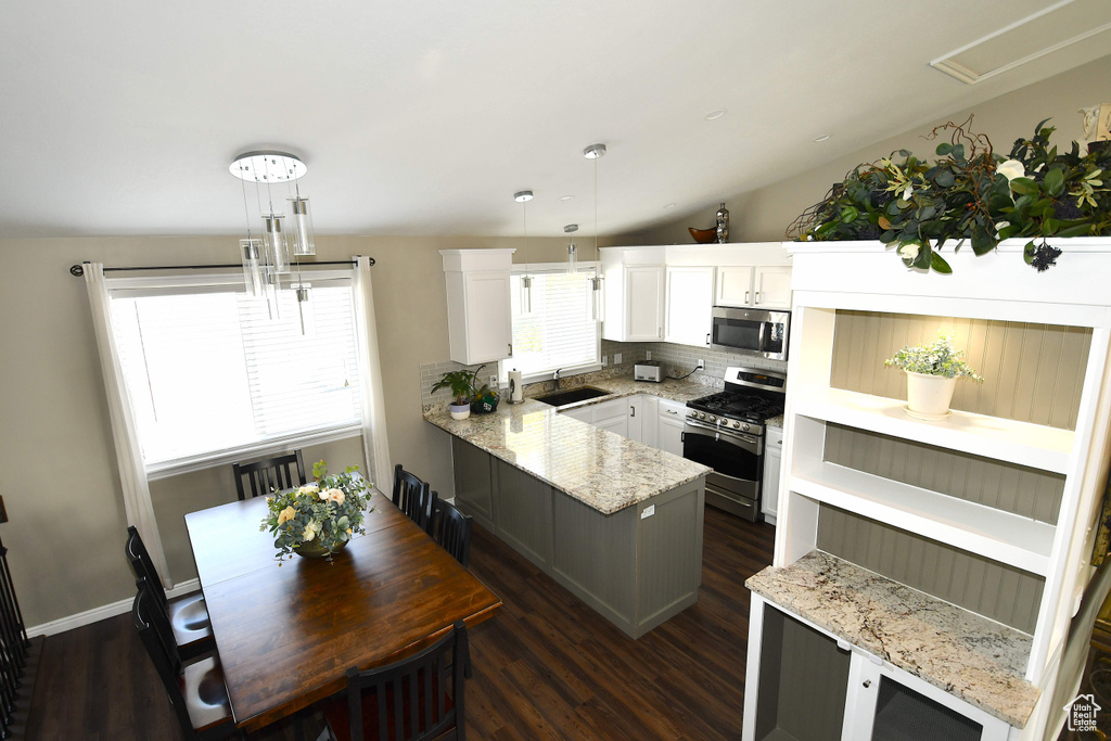 Kitchen with white cabinets, vaulted ceiling, sink, decorative light fixtures, and stainless steel appliances