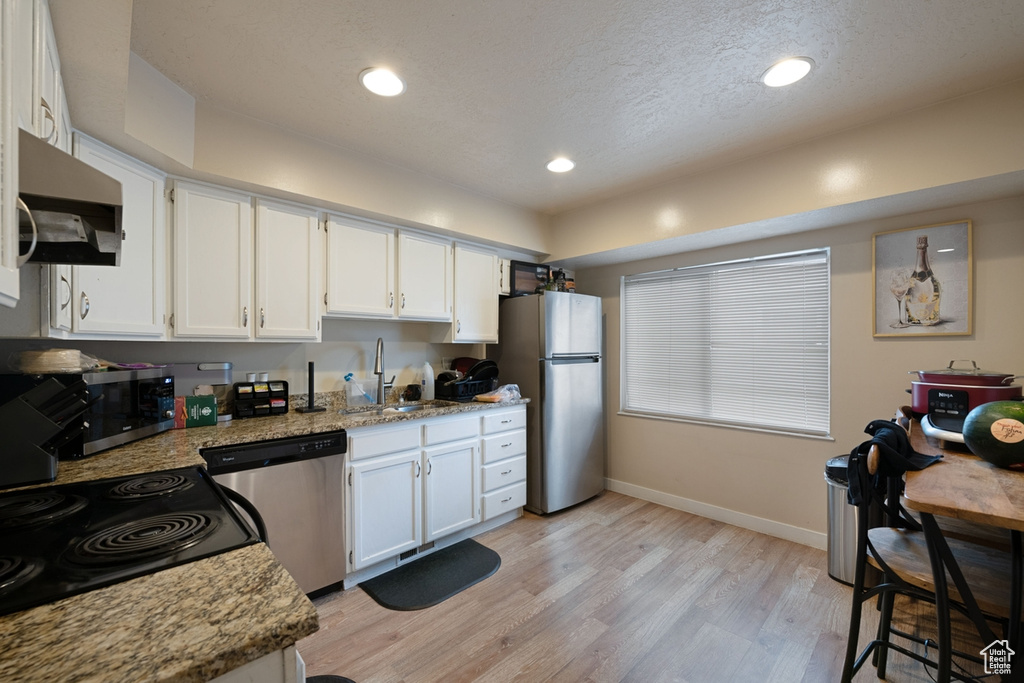 Kitchen featuring sink, stainless steel appliances, white cabinetry, and light hardwood / wood-style flooring