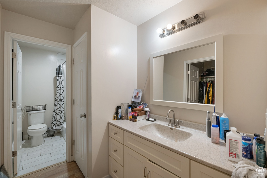 Bathroom featuring hardwood / wood-style floors, toilet, vanity, and curtained shower