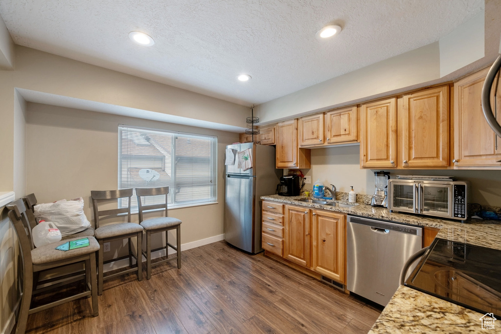 Kitchen with appliances with stainless steel finishes, dark wood-type flooring, a textured ceiling, and light stone countertops