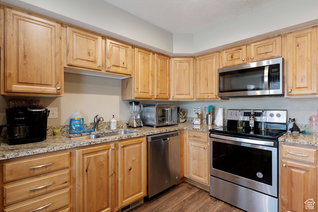 Kitchen featuring light brown cabinets, appliances with stainless steel finishes, light stone counters, hardwood / wood-style flooring, and sink