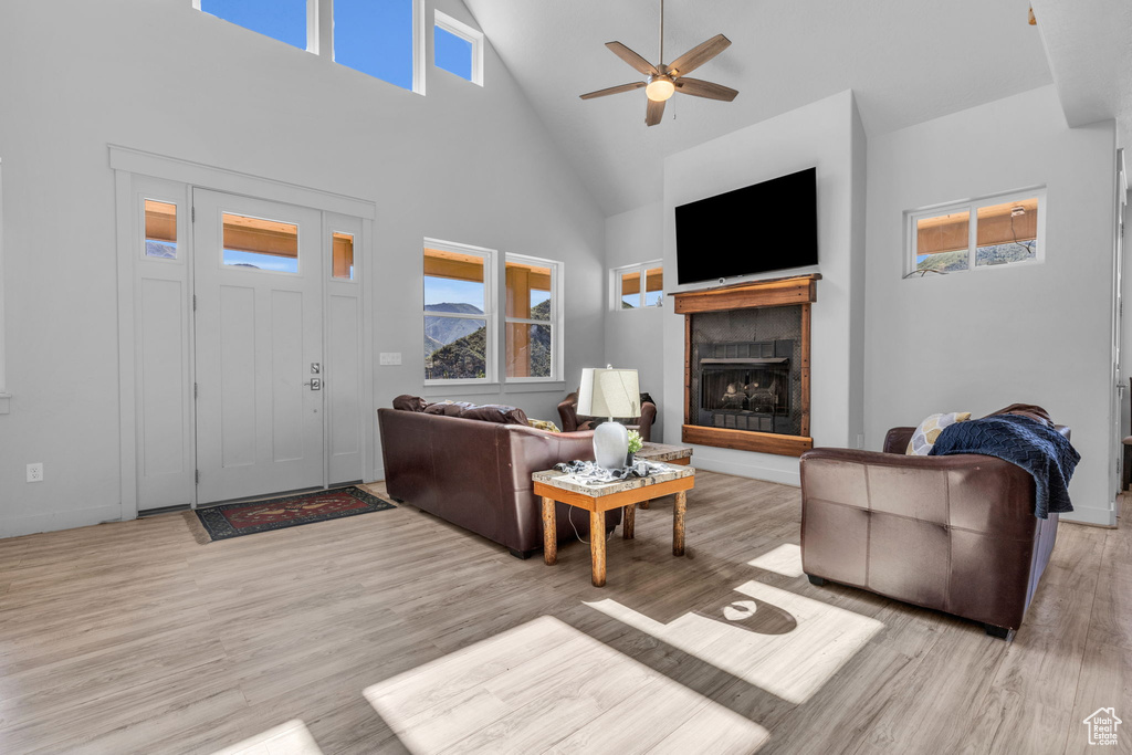 Living room featuring ceiling fan, high vaulted ceiling, light hardwood / wood-style flooring, and a tile fireplace