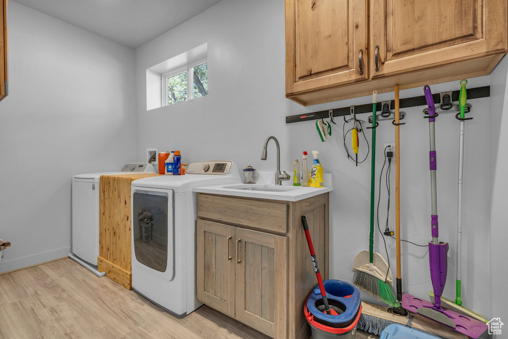 Clothes washing area with light wood-type flooring, sink, independent washer and dryer, and cabinets