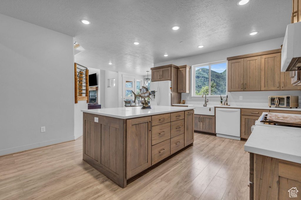 Kitchen featuring a center island, sink, white appliances, light hardwood / wood-style floors, and a textured ceiling