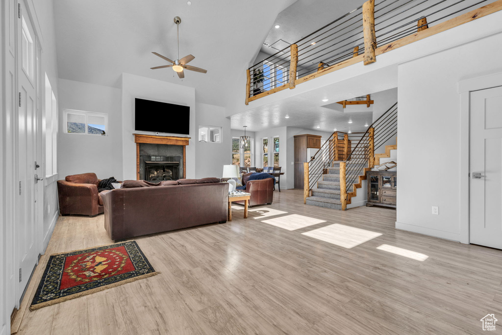 Living room with light hardwood / wood-style floors, high vaulted ceiling, a tiled fireplace, and ceiling fan