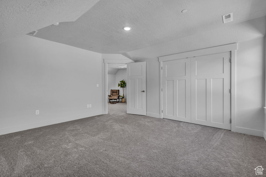 Unfurnished bedroom with a textured ceiling, lofted ceiling, and light carpet