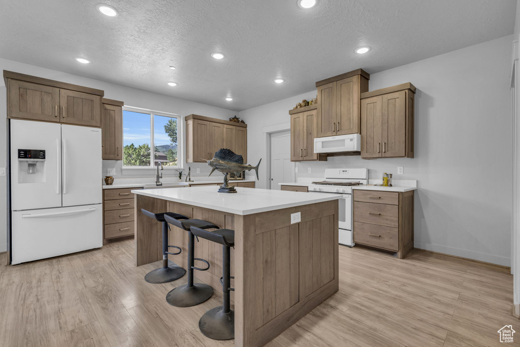 Kitchen featuring white appliances, light hardwood / wood-style floors, a textured ceiling, a kitchen island, and a breakfast bar area