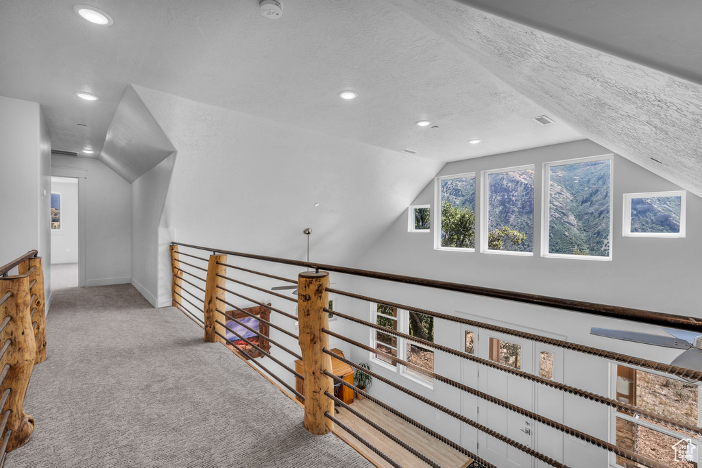 Corridor with vaulted ceiling, carpet, and a textured ceiling