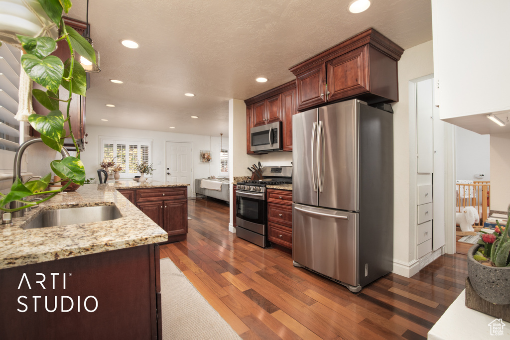 Kitchen featuring kitchen peninsula, light stone counters, appliances with stainless steel finishes, and dark wood-type flooring