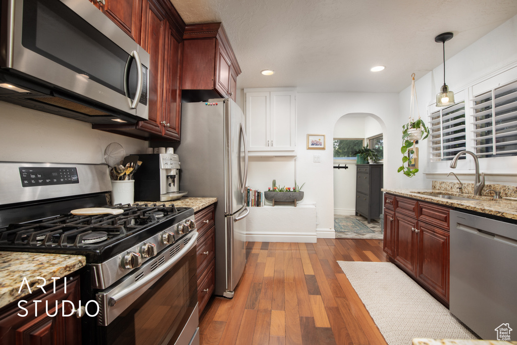 Kitchen featuring sink, decorative light fixtures, light stone countertops, light hardwood / wood-style floors, and stainless steel appliances