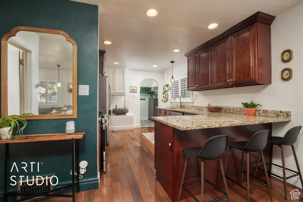 Kitchen with dark wood-type flooring, hanging light fixtures, a breakfast bar, light stone countertops, and kitchen peninsula