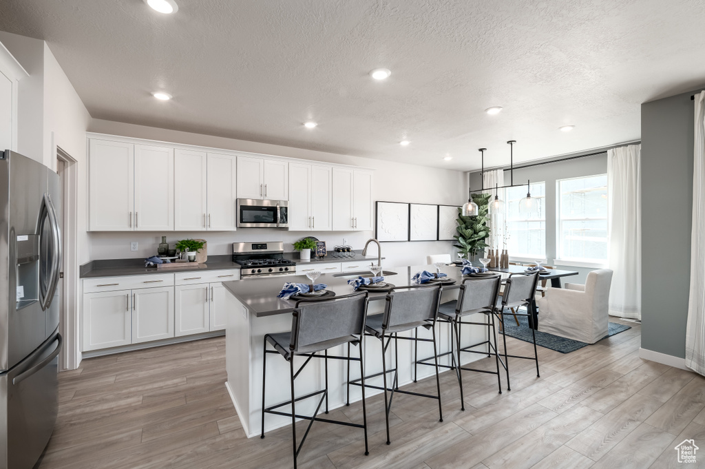 Kitchen with a kitchen breakfast bar, light hardwood / wood-style flooring, an island with sink, stainless steel appliances, and white cabinets