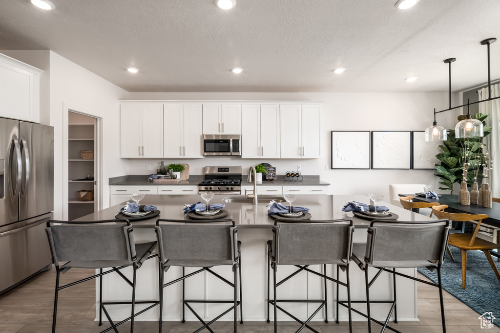 Kitchen featuring appliances with stainless steel finishes, light hardwood / wood-style floors, a kitchen bar, sink, and a kitchen island with sink