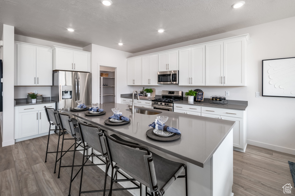 Kitchen featuring stainless steel appliances, a kitchen island with sink, a breakfast bar, and light wood-type flooring