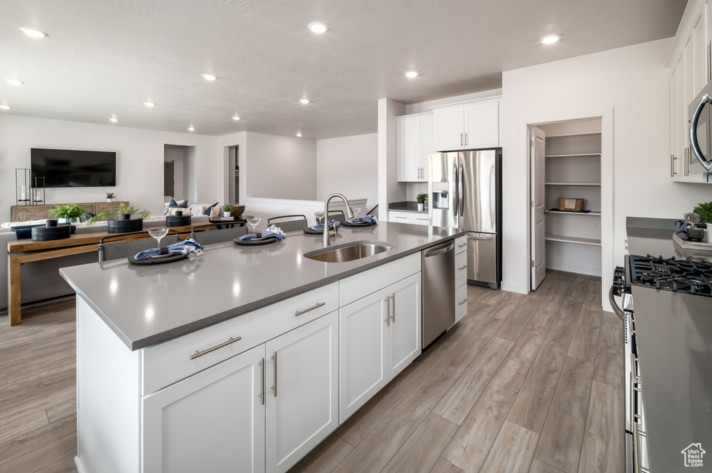 Kitchen with light hardwood / wood-style flooring, an island with sink, white cabinets, sink, and stainless steel appliances