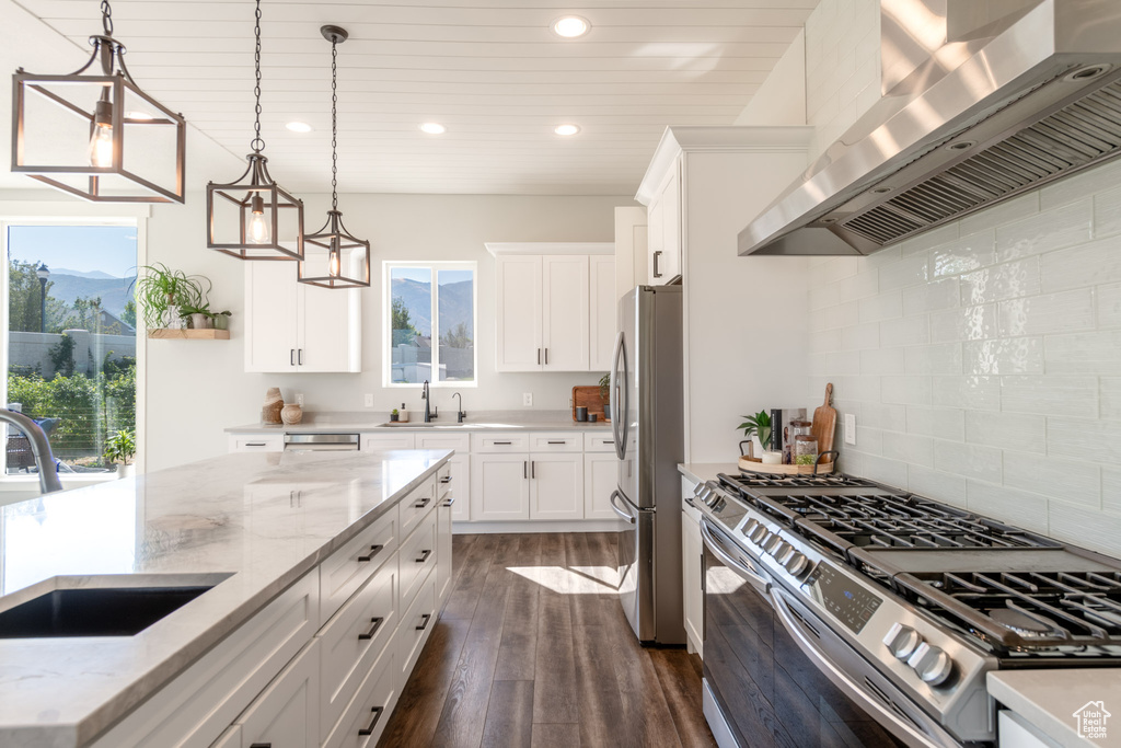 Kitchen featuring white cabinets, decorative light fixtures, stainless steel appliances, wall chimney range hood, and dark hardwood / wood-style floors