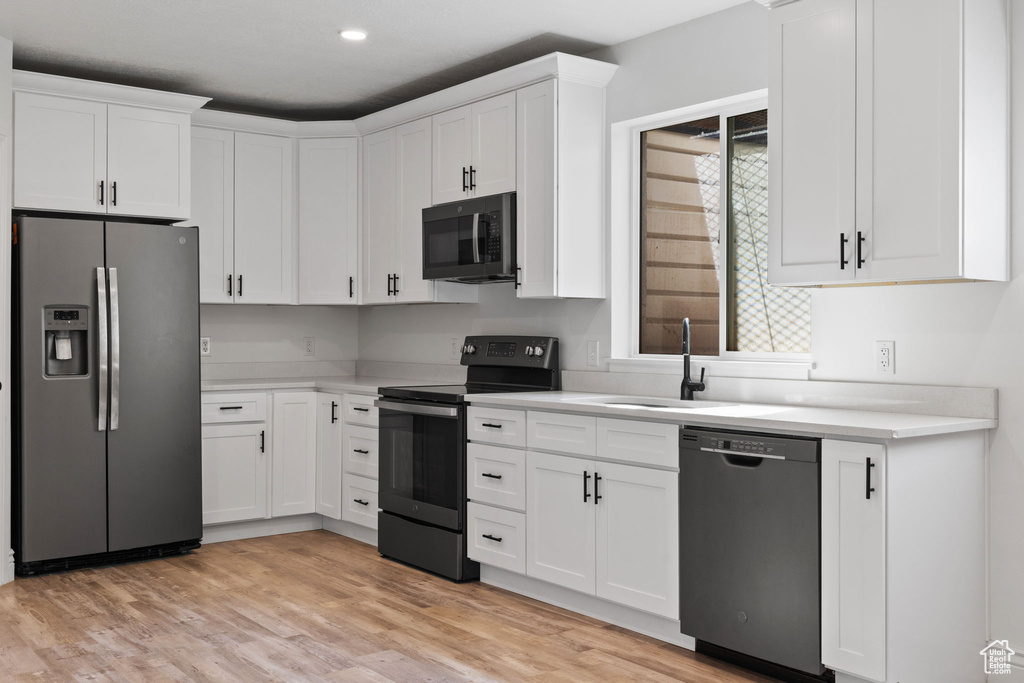 Kitchen with light wood-type flooring, white cabinetry, stainless steel appliances, and sink