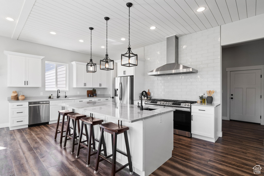 Kitchen featuring wall chimney exhaust hood, appliances with stainless steel finishes, dark hardwood / wood-style flooring, and a center island with sink