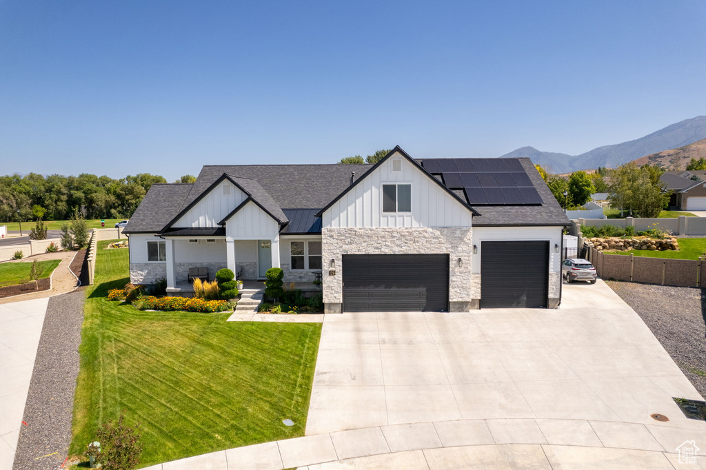 Modern farmhouse style home with a mountain view, solar panels, a front yard, and a garage