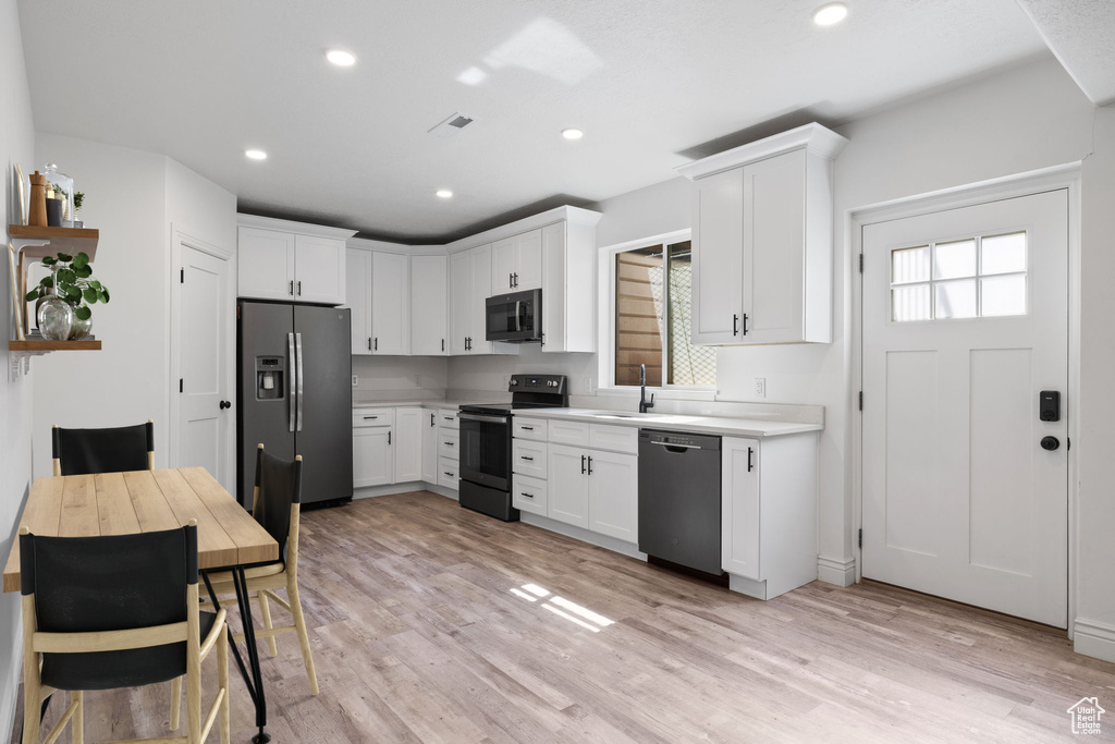 Kitchen with black appliances, sink, light wood-type flooring, and white cabinets