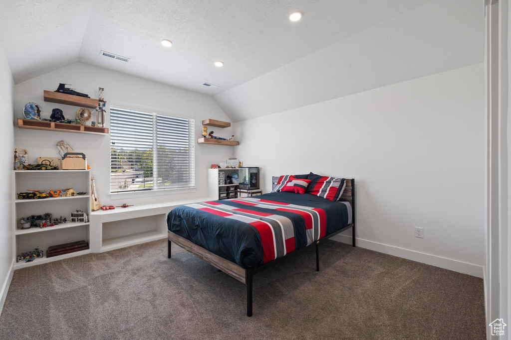 Bedroom featuring a textured ceiling, dark carpet, and vaulted ceiling