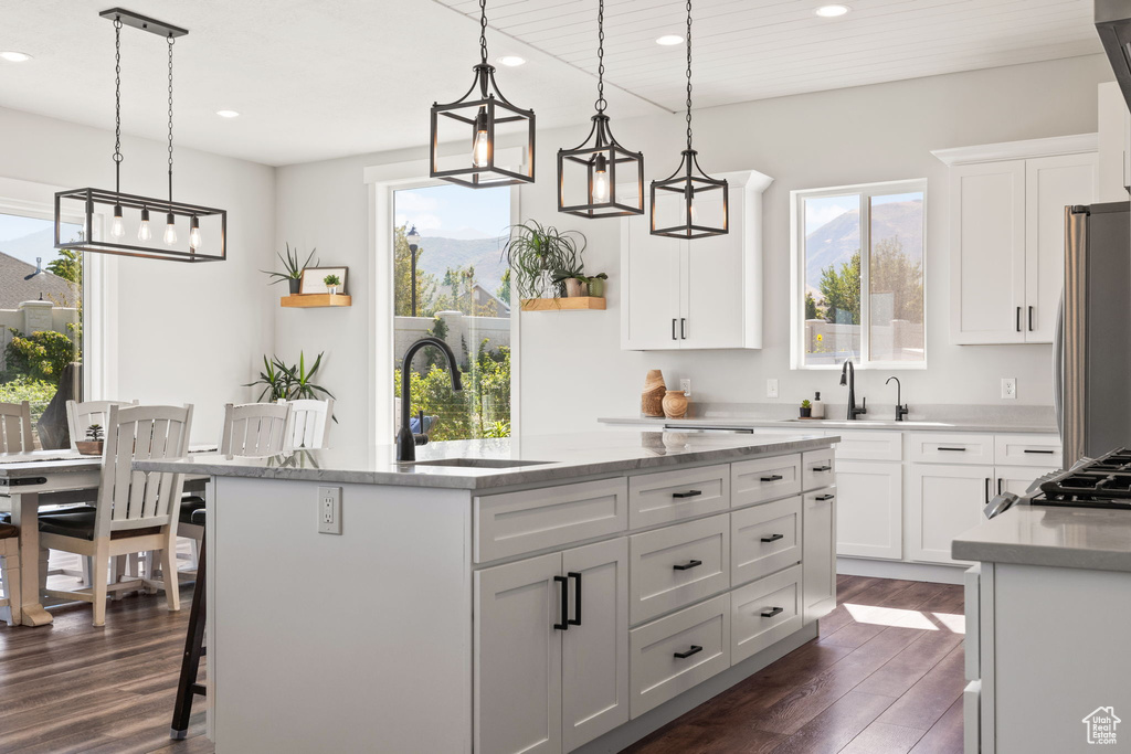 Kitchen featuring a kitchen island with sink, pendant lighting, dark hardwood / wood-style flooring, and stainless steel refrigerator