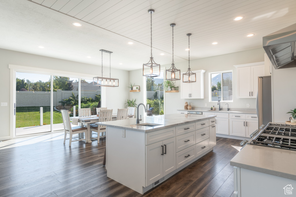 Kitchen featuring white cabinets, hanging light fixtures, sink, dark wood-type flooring, and a kitchen island with sink