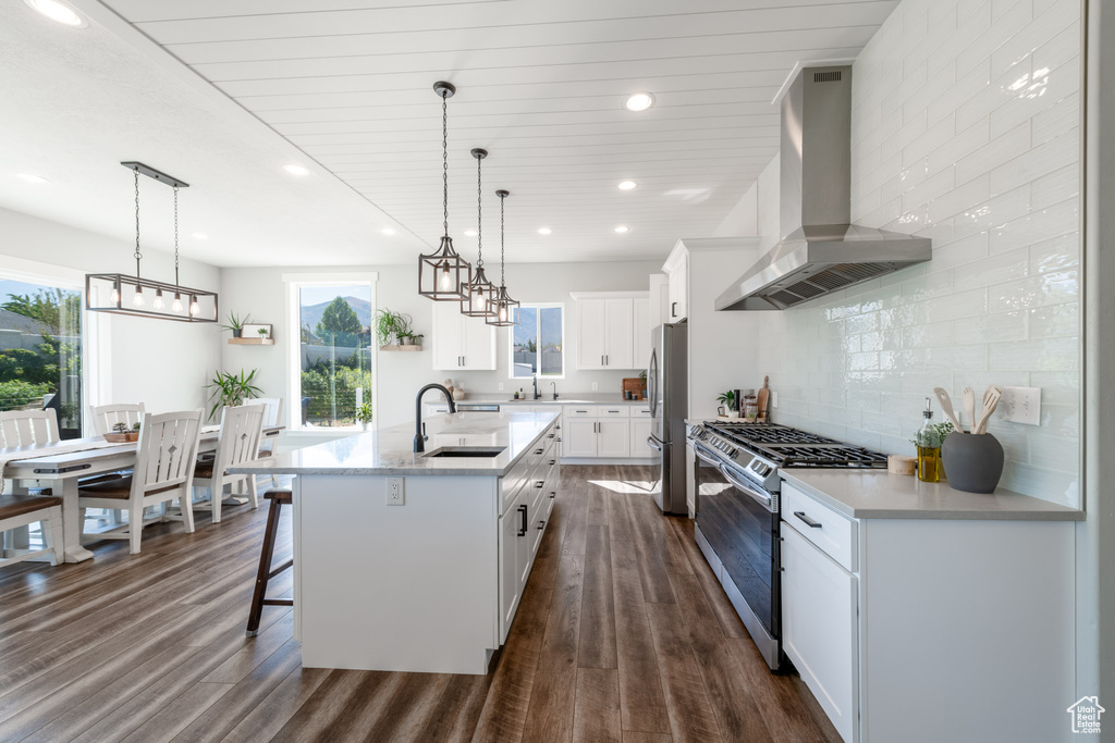 Kitchen with dark hardwood / wood-style floors, wall chimney exhaust hood, appliances with stainless steel finishes, a kitchen island with sink, and sink