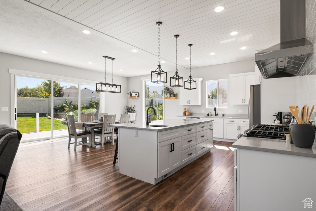 Kitchen featuring dark hardwood / wood-style floors, white cabinetry, a center island with sink, and wall chimney range hood