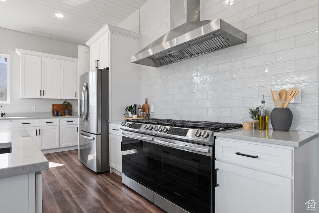 Kitchen with backsplash, appliances with stainless steel finishes, dark wood-type flooring, wall chimney range hood, and white cabinets