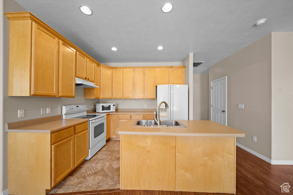 Kitchen with sink, light wood-type flooring, an island with sink, and white appliances