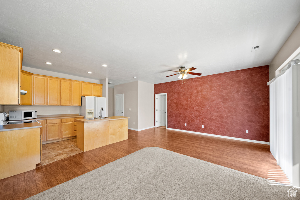 Kitchen with light tile patterned flooring, white appliances, light brown cabinetry, a kitchen island with sink, and ceiling fan