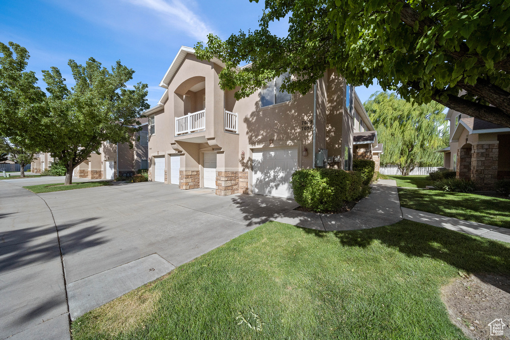 View of front facade featuring a balcony, a front lawn, and a garage