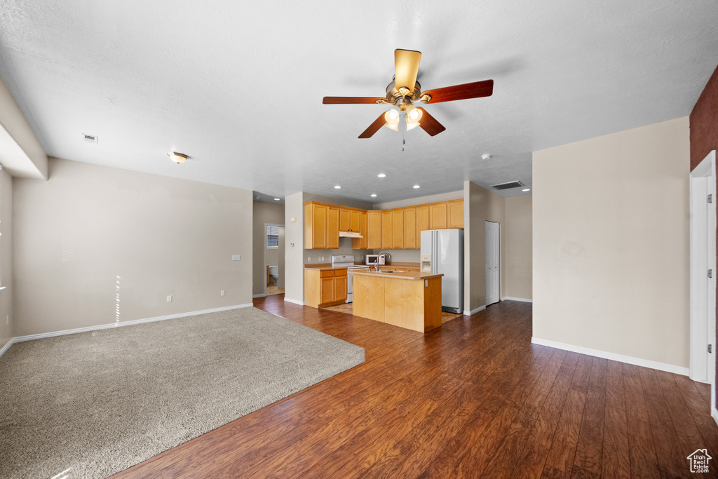 Kitchen with dark hardwood / wood-style flooring, a center island with sink, white appliances, and ceiling fan