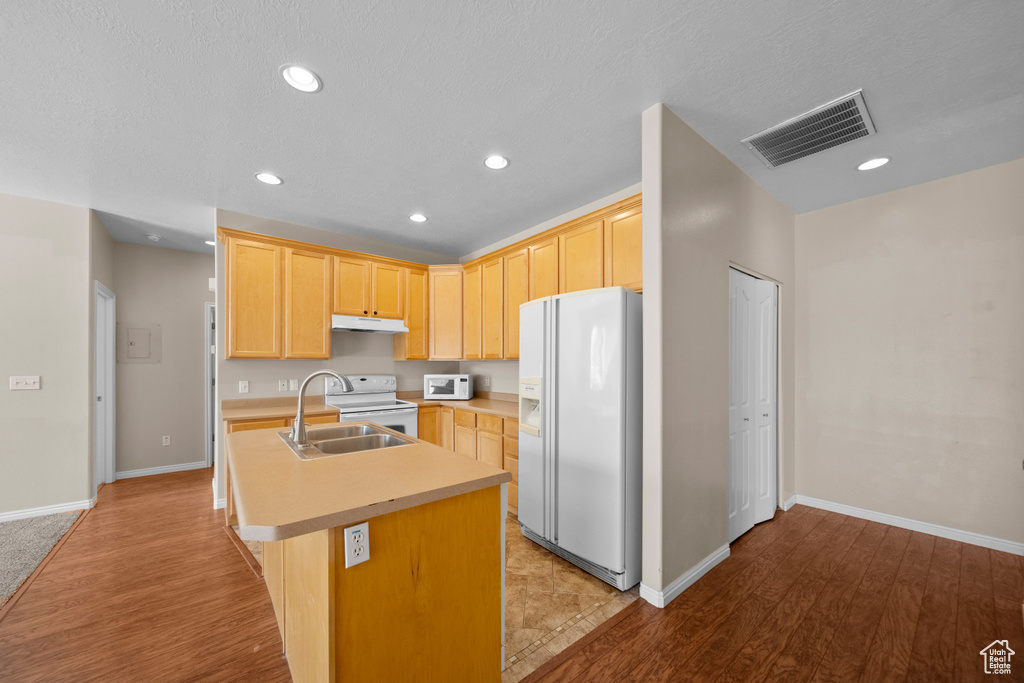 Kitchen featuring sink, light wood-type flooring, a center island with sink, and white appliances