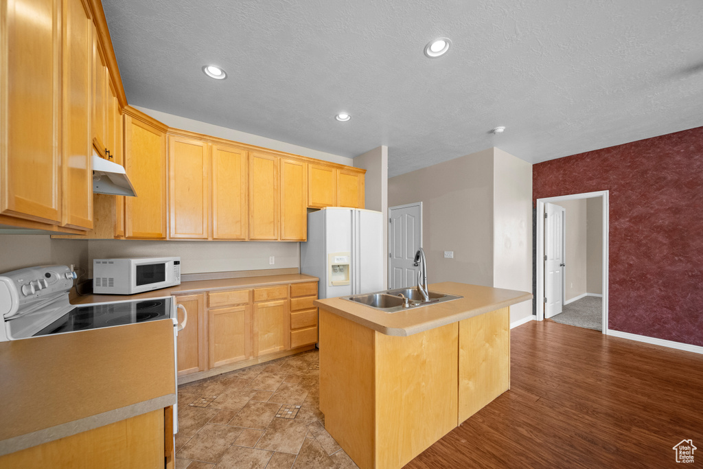 Kitchen with sink, white appliances, light hardwood / wood-style floors, light brown cabinets, and a center island with sink