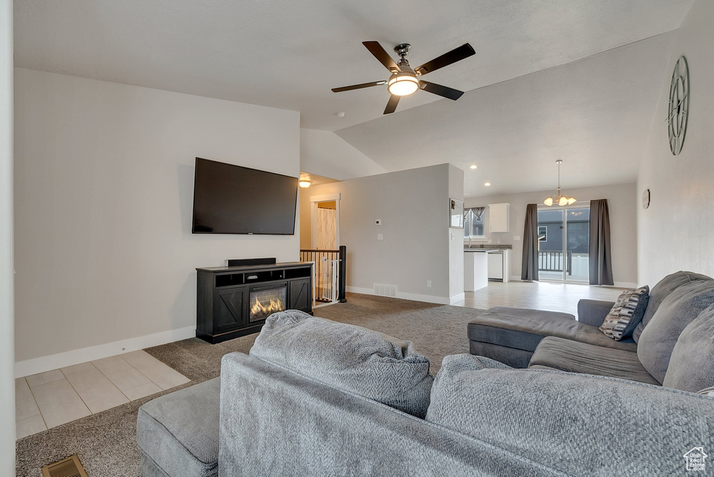 Tiled living room featuring a fireplace, lofted ceiling, and ceiling fan with notable chandelier