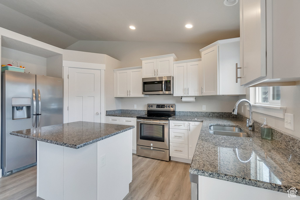 Kitchen featuring stainless steel appliances, lofted ceiling, white cabinets, and a center island