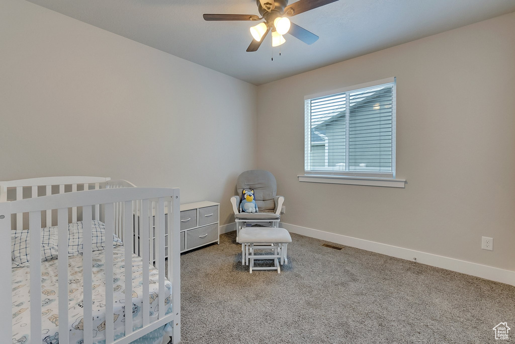 Bedroom featuring ceiling fan, a crib, and carpet floors