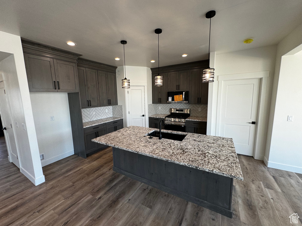 Kitchen featuring decorative backsplash, dark brown cabinetry, a kitchen island with sink, hardwood / wood-style floors, and stainless steel appliances