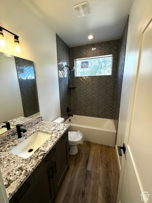 Full bathroom featuring hardwood / wood-style floors, tiled shower / bath, toilet, and vanity