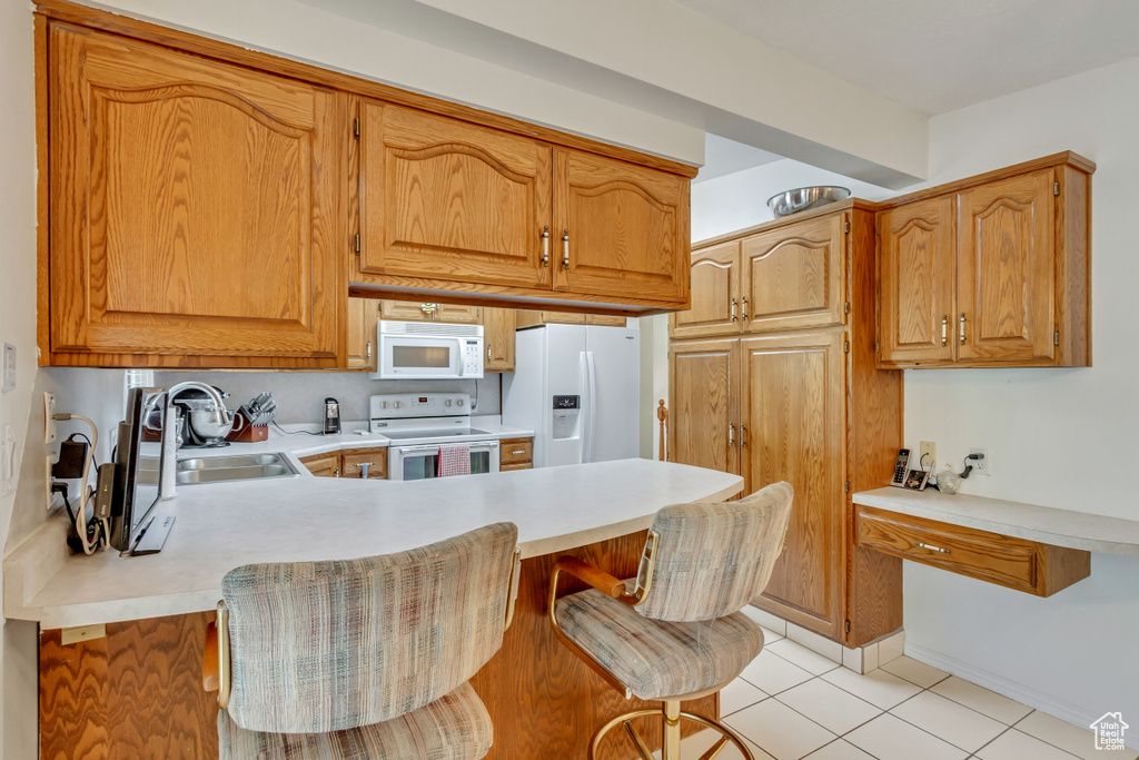 Kitchen with kitchen peninsula, light tile patterned floors, sink, a breakfast bar area, and white appliances