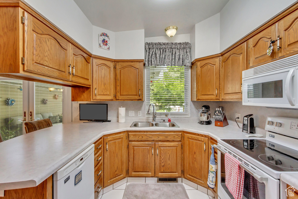 Kitchen featuring sink, kitchen peninsula, light tile patterned flooring, and white appliances