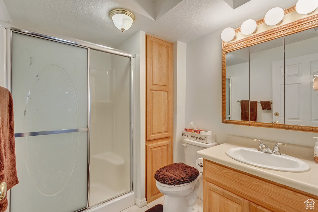 Bathroom with a textured ceiling, an enclosed shower, toilet, and vanity